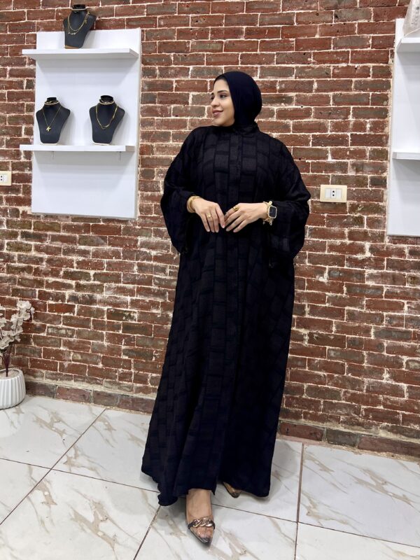 Woman in black dress against brick wall.